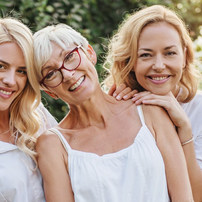Three smiling women in a sunny garden.