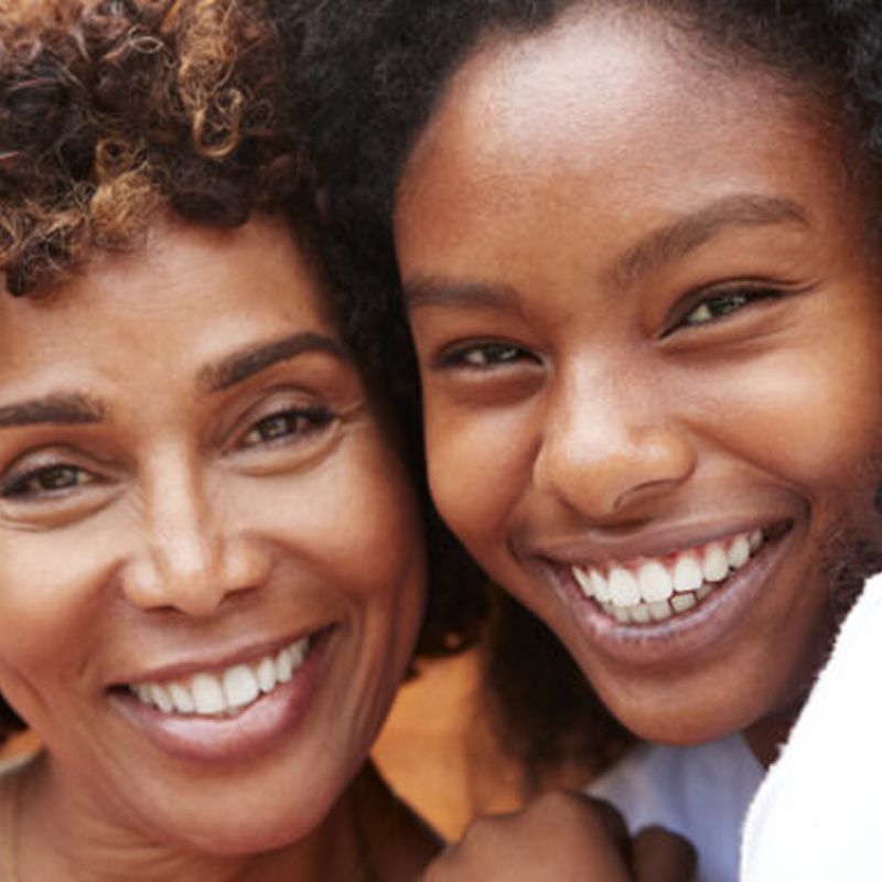 Smiling woman and girl embracing outdoors.