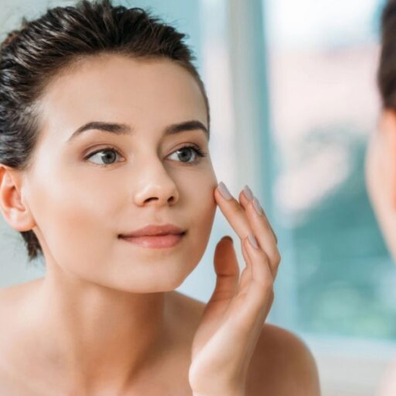 Woman applying skincare in front of mirror.