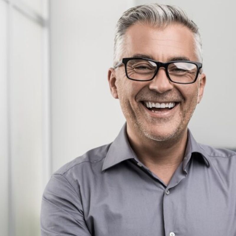 Smiling man in a gray shirt and glasses.