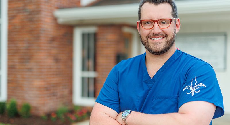 Smiling healthcare professional in blue scrubs outdoors.