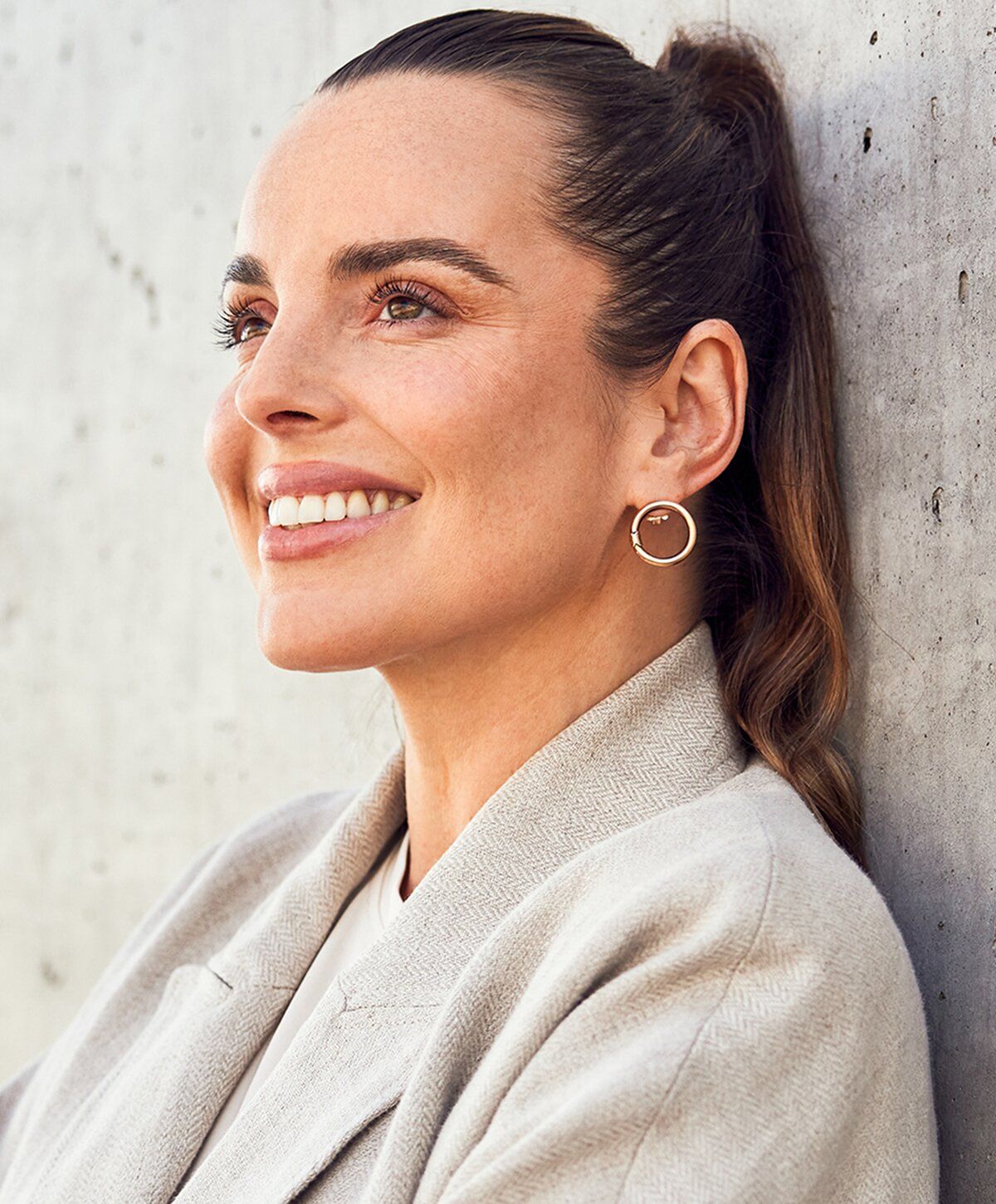 Smiling woman with stylish earrings against concrete background.