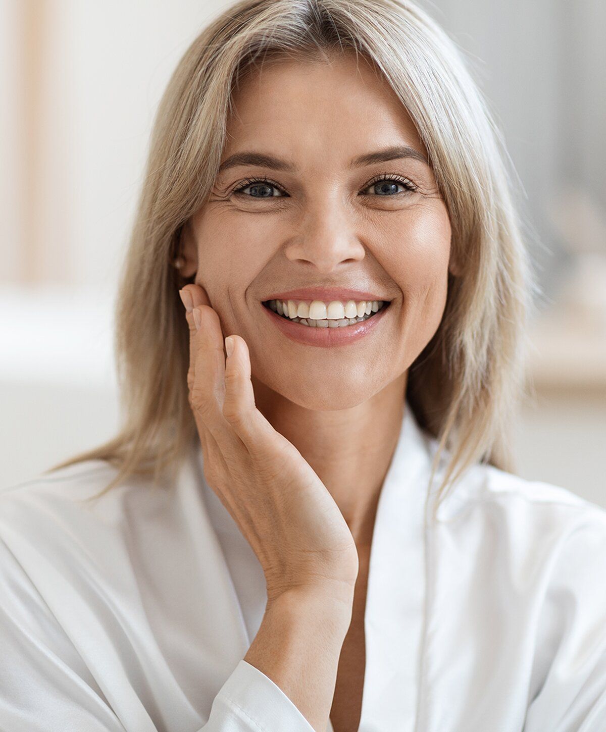Smiling woman touching her face in a white robe.