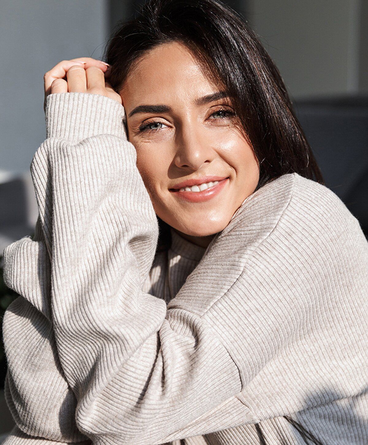 Woman smiling in cozy sweater, soft lighting.