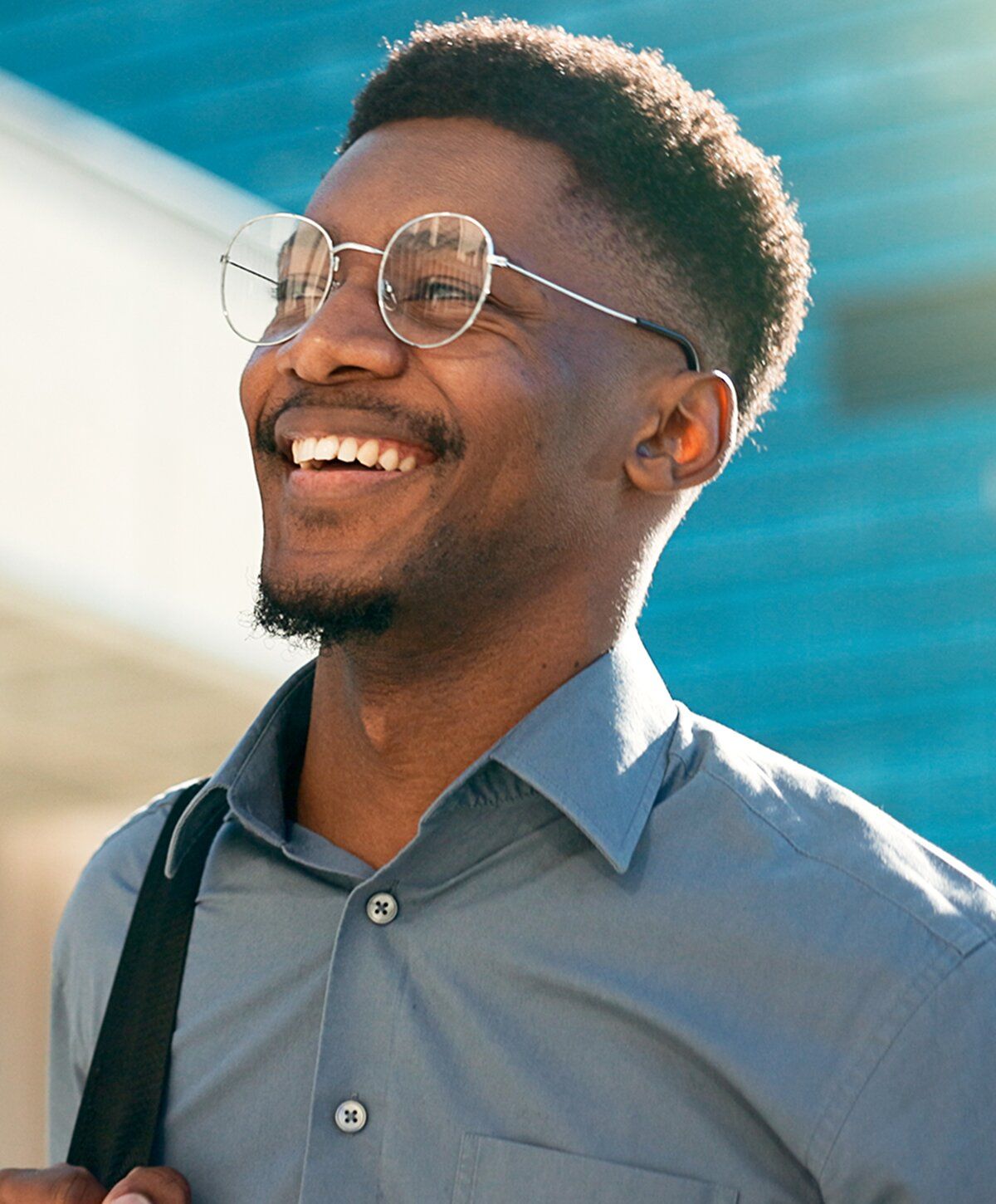 Smiling man wearing glasses outdoors, sunny background.