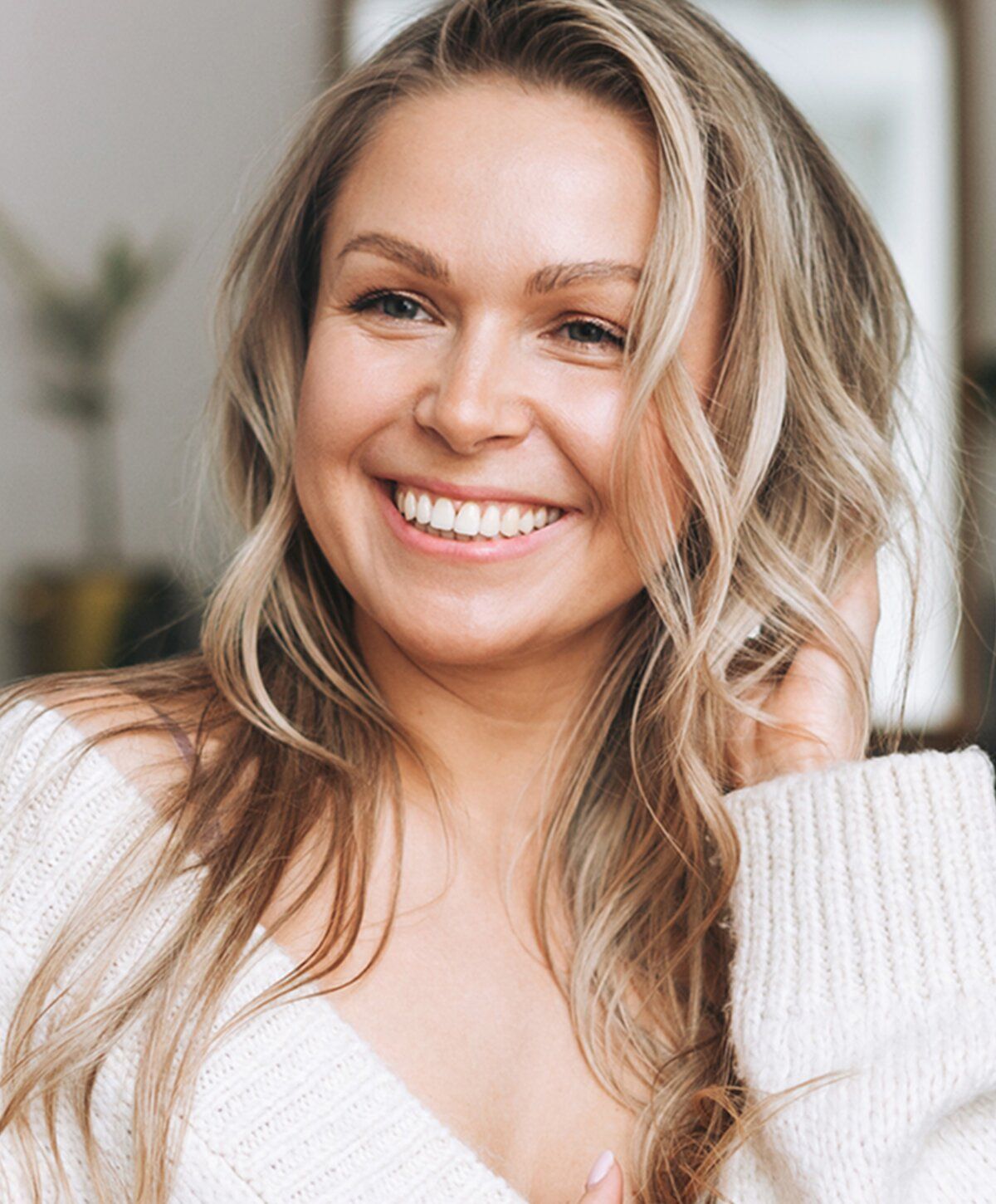 Smiling woman with long wavy hair in sweater.