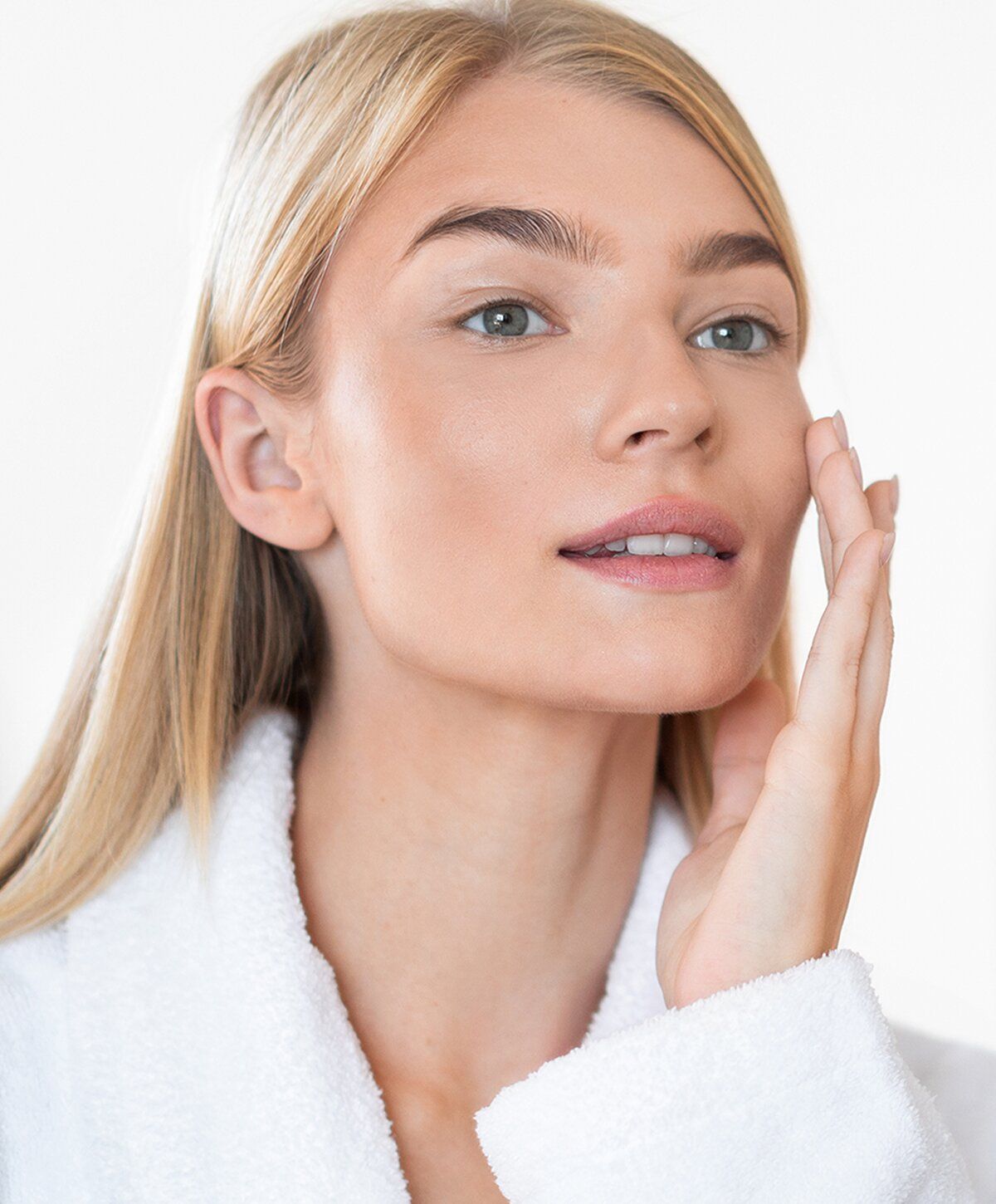 Woman applying skincare in a white robe.