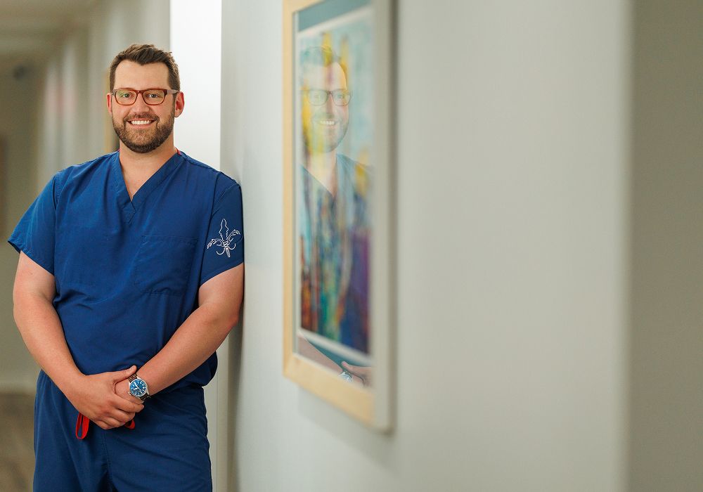 Smiling healthcare professional in scrubs, hallway setting.