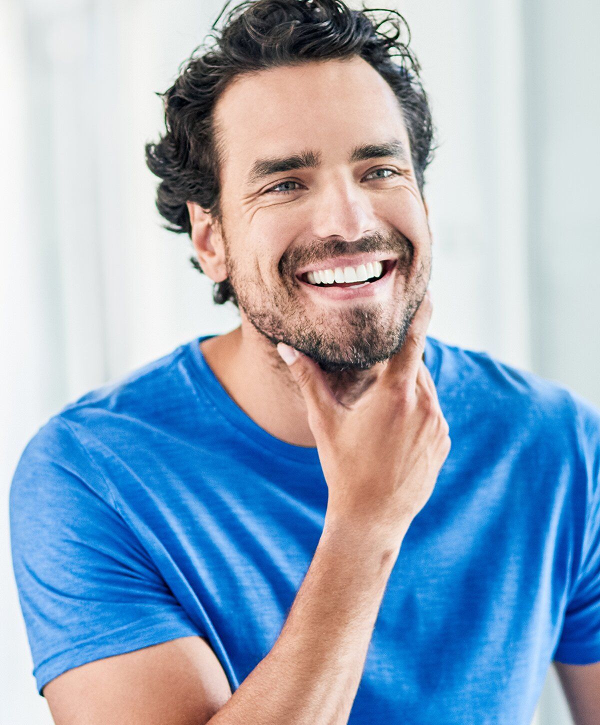 Smiling man in a blue shirt, hand on chin.