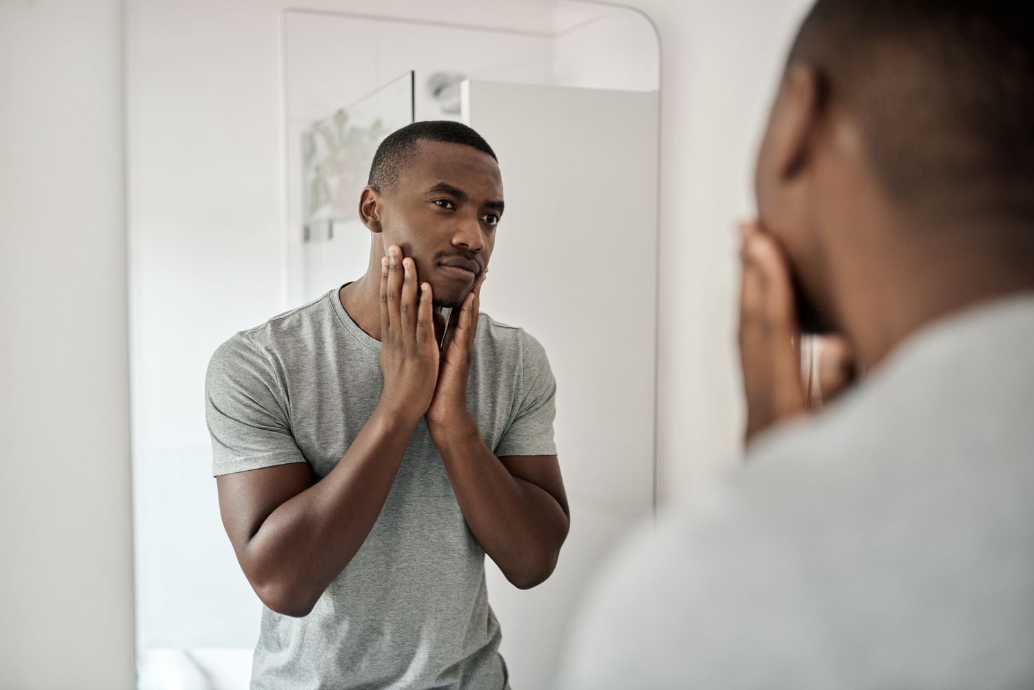 Man inspecting skin in bathroom mirror.